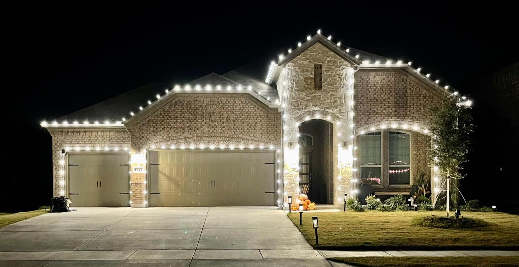 Brick home with warm white lights across the roofline and garage